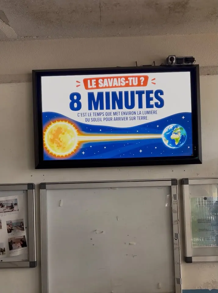 Écran extérieur fixé au mur d'un collège, affichant une rubrique « Le savais-tu ? » sur la lumière du Soleil
